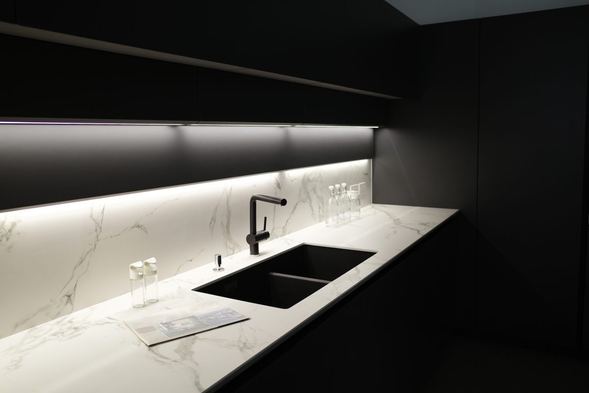 An image of black cabinetry under cabinet lighting and a sink in a marble countertop underneath the cabinets.