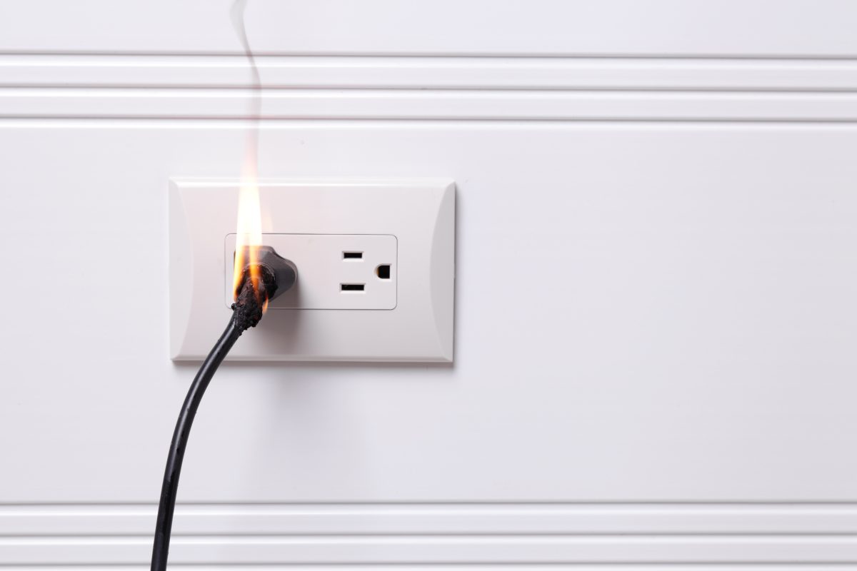 An image of a black cord plugged into an electrical socket, and the cord is on fire.