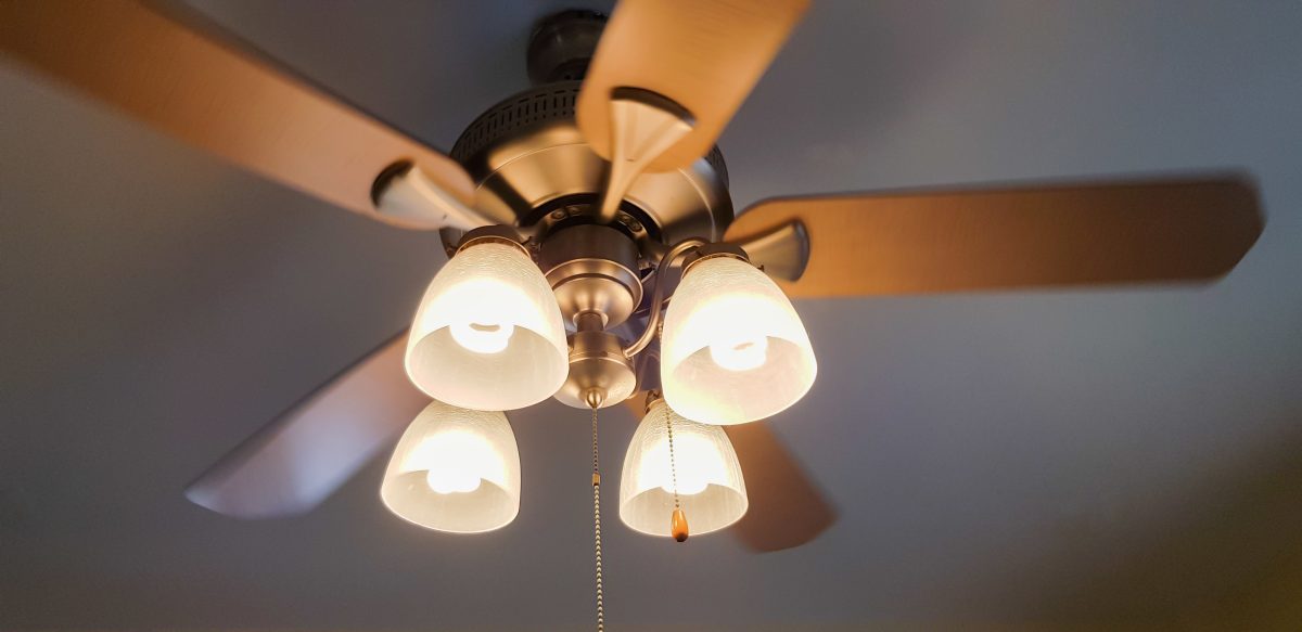 A wooden ceiling fan with four lights in the center and metal pull strings.